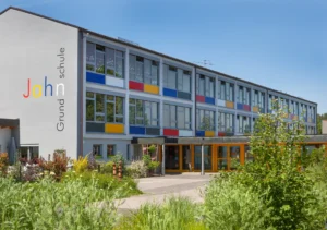 Jahn Grundschule in Rosenberg mit modernem Gebäude, farbigen Fensterfeldern in Rot, Blau und Gelb, Eingangstrakt mit Holzverkleidung und begrüntem Vorplatz