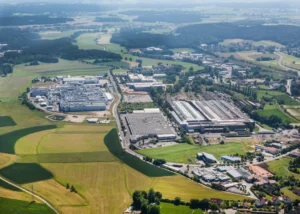 Luftaufnahme zeigt Sulzbach-Rosenberg mit mehreren Industriegebäuden und Produktionshallen, dichten Wohngebieten, Waldgebieten, grünen Wiesen und landwirtschaftlichen Feldern in hügeligem Terrain
